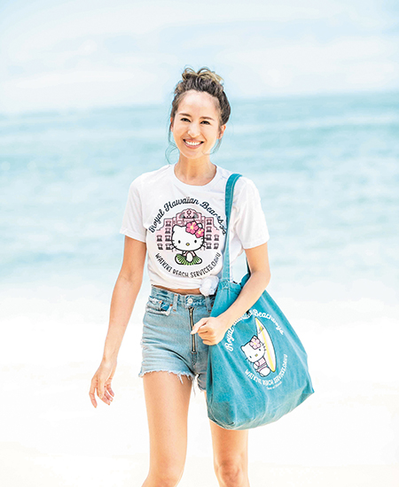 female model wearing a Royal Hawaiian x Hello Kitty collaboration white t-shirt and also holding a Hello Kitty collab demin bag
