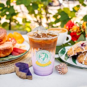 Latte in a cup with latte art, surrounded by kona coffee beans and plumeria flowers