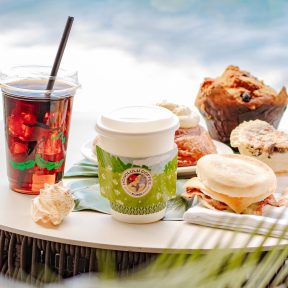 iced and hot coffee drinks from Honolulu Coffee on a table by the ocean with some sweet pastries on the side