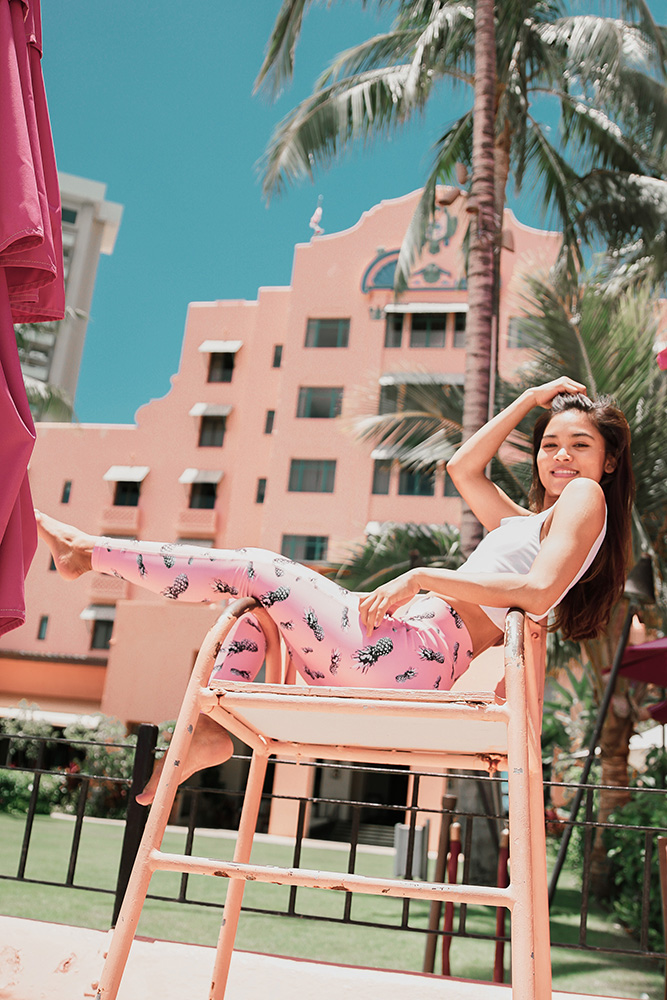 Female lounging in a chair wearing pink yoga leggings and a white spaghetti strap top